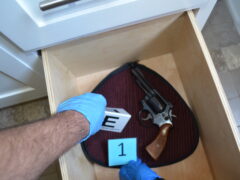 box with a revolver in it and gloved hands placing evidence markers