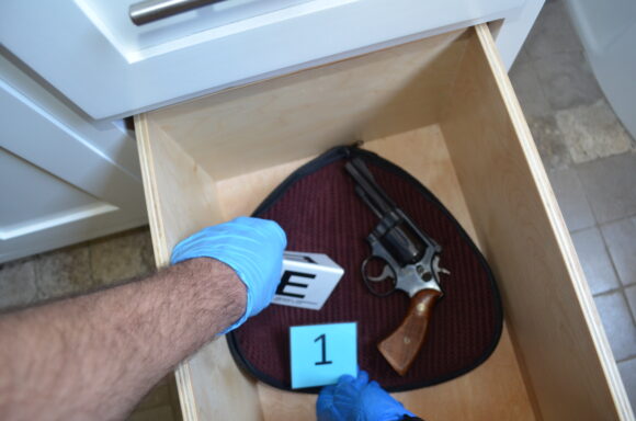 box with a revolver in it and gloved hands placing evidence markers