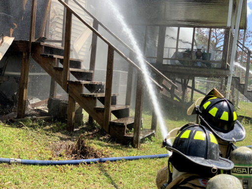 Firefighters Crouched Down Spraying Home with Water Hose