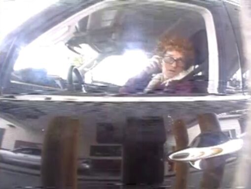 A white male believed involved in multiple "smash and grab" burglaries is observed in surveillance video wearing a wig and glasses.