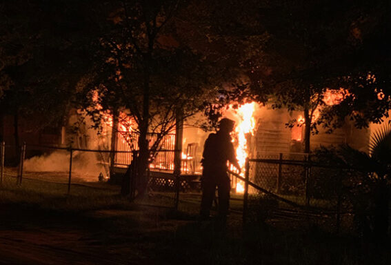 Firefighter holding host in front of burning home