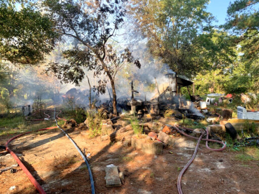 smoke coming from pile of what's left of a mobile home after a structure fire