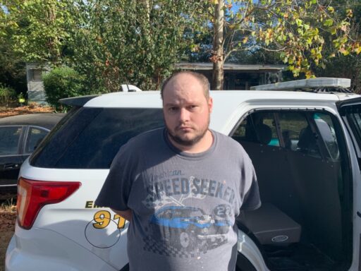 A man in handcuffs in front of a patrol car.