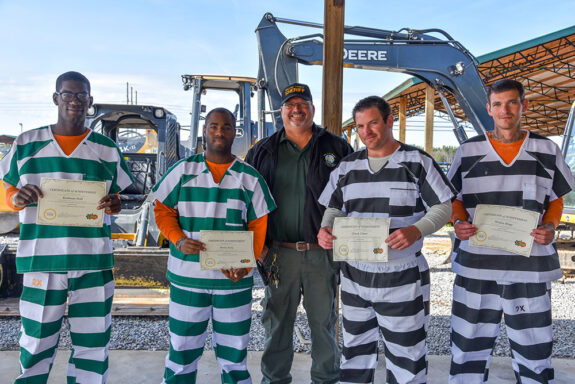 Four inmates holding up their heavy equipment certificates at walton county jail graduation ceremony