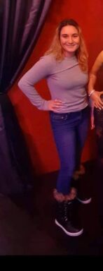 Photo of white female in blue jeans, boots and a long sleeve pink shirt.