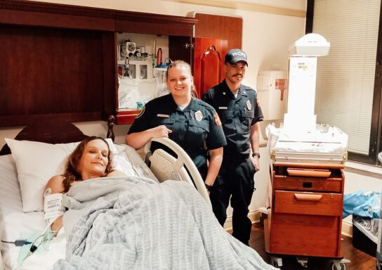 Mother in hospital bed with a paramedic and EMT smiling standing next to her
