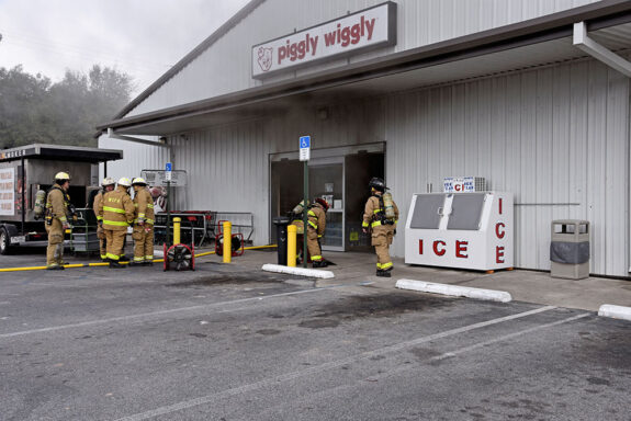 Firefighters working out front of a Piggly Wiggly with smoke coming out