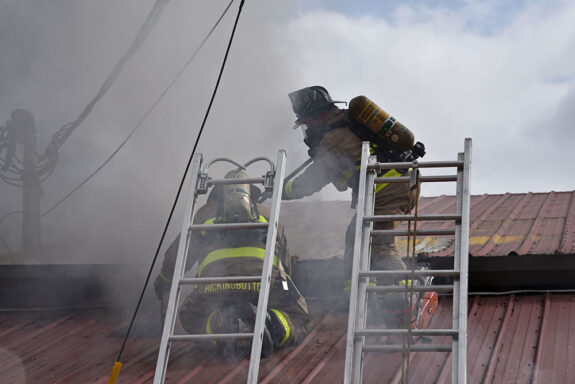 Firefighters using chainsaw on metal roof