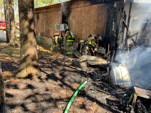 Firefighters cutting into the side of a single wide mobile home with structure fire damage