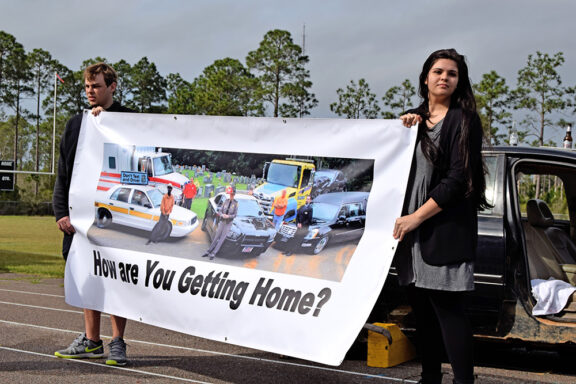 Male and female teenager holding a banner that reads "how are you getting home?"