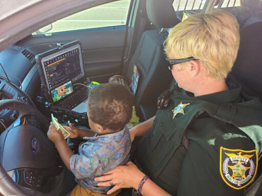 A female deputy with a child on her lap in a patrol car watching cartoons.