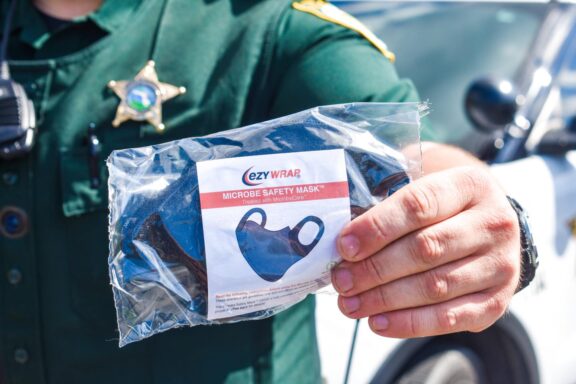 Sheriff's deputy in green uniform holding a black safety face mask