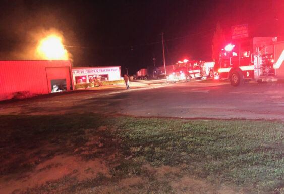 fire trucks outside of an auto parts store that has flames coming from it