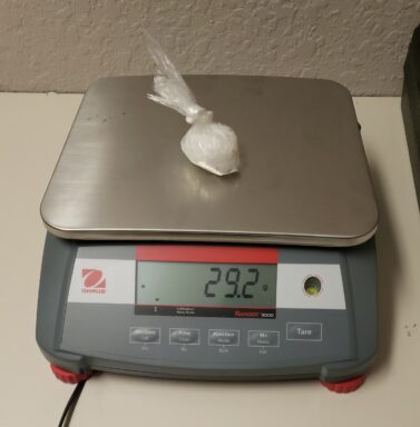 A scale with a small plastic bag on top of it with a white crystal substance inside.