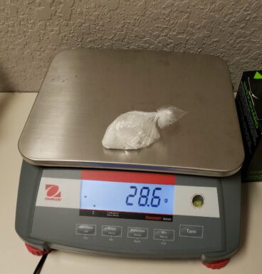 A scale with a small plastic bag on top of it with a white crystal substance inside.