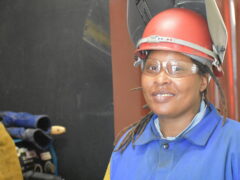 A woman smiles wearing a welding helmet.