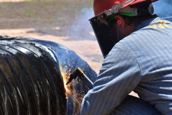 A woman welds cut in a pipe.
