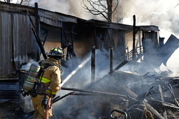 Firefighter spraying water on a home with smoke coming out of it