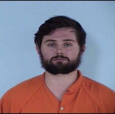 Mug shot of a white male wearing an orange jumpsuit with a beard.