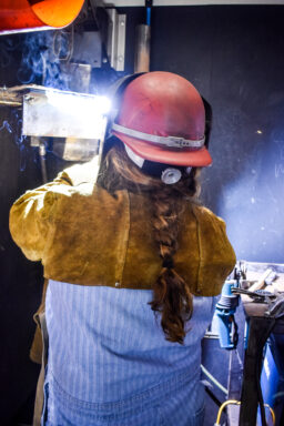 A woman with a long braid welds with a helmet.