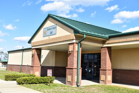 A brick building with a green roof with a sign that reads, "Walton County Jail".