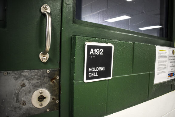 A black sign that reads, 'holding cell' posted on a green brick wall with a door beside it.