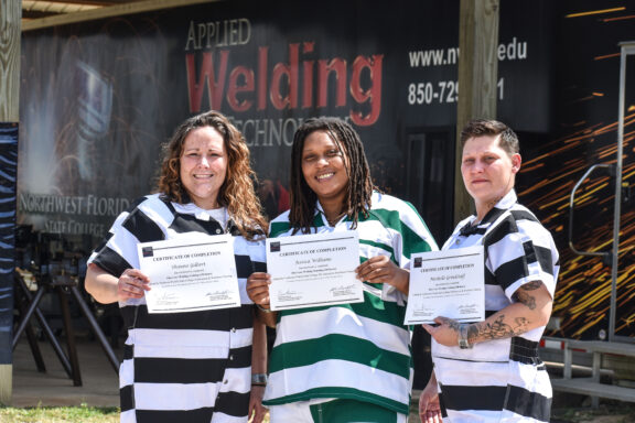 A group of three female inmates stand and smile as they hold certificates.