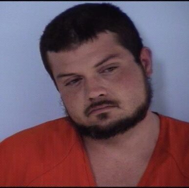 Mug shot of white male with facial hair in an orange jumpsuit.