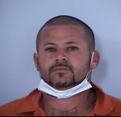 Mug shot of white male with facial hair and a mask hanging below his chin.