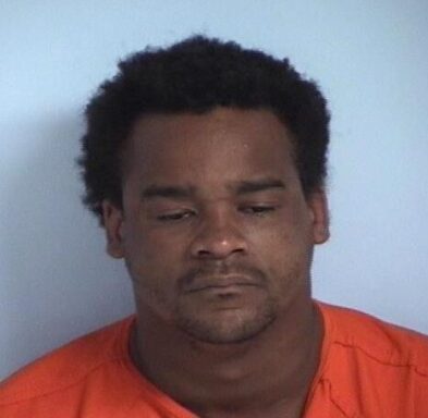 Mug shot of a black male in an orange jumpsuit with a short afro. 