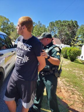 White male in a navy blue shirt being cuffed by Walton County Sheriff's Office deputy