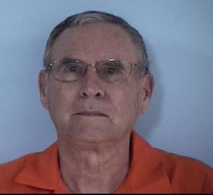 Mug shot of an older white male with glasses and white hair.