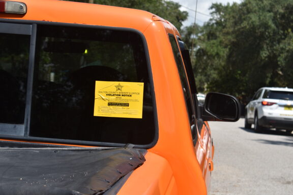 A yellow violation sticker on the back windshield of an orange truck.