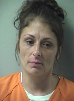 Mugshot of a white female with brown hair in a bun wearing an orange jumpsuit
