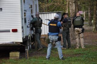 Four men in ballistic vests and shields knocking on the door of a trailer.