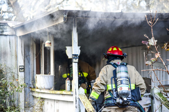 firefighters entering into a burning mobile home with smoke coming from the roof