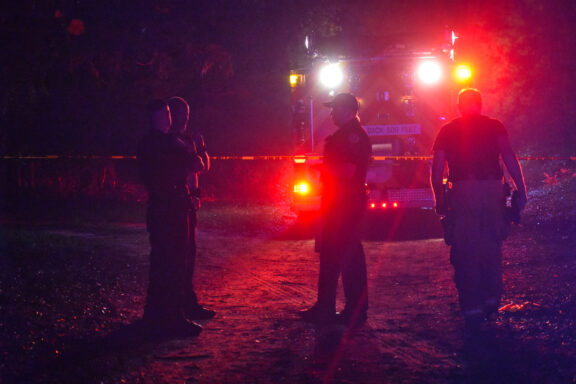 Fire responders standing in front a fire truck with lights on at night