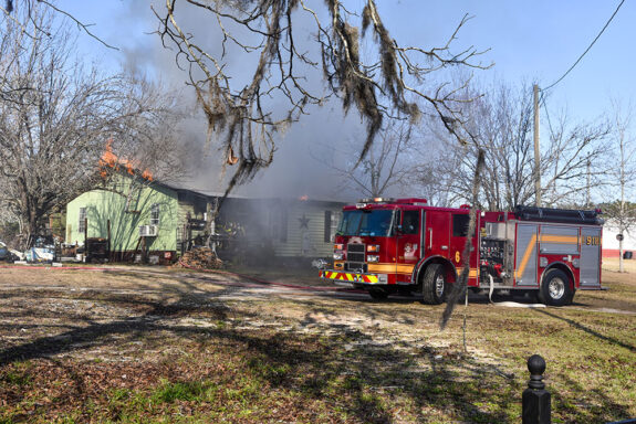 Fire truck parked in front of a light green home that is on fire