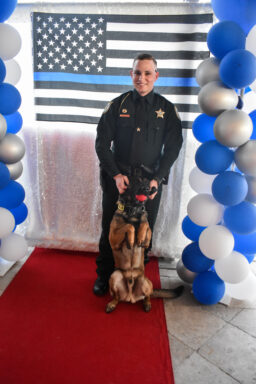 Deputy and K-9 posing in front of a Thin Blue Line flag