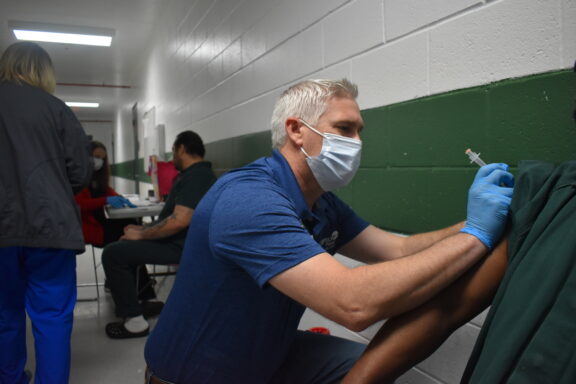 Doctor in mask administering shot in patients arm