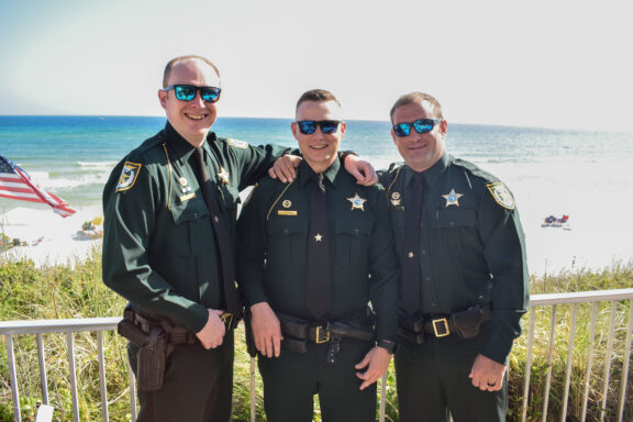 Three deputies in uniform smiling in front of the beach.