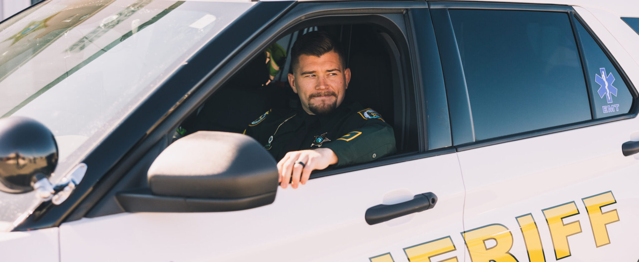 White male law enforcement officer sitting in sheriff car