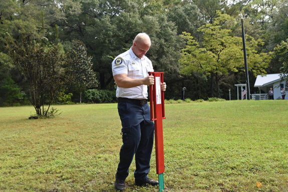 White male wearing fire officer uniform installing address sign in yard