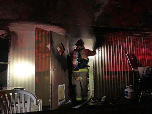 Firefighter standing in doorway of mobile home with smoke coming out of home