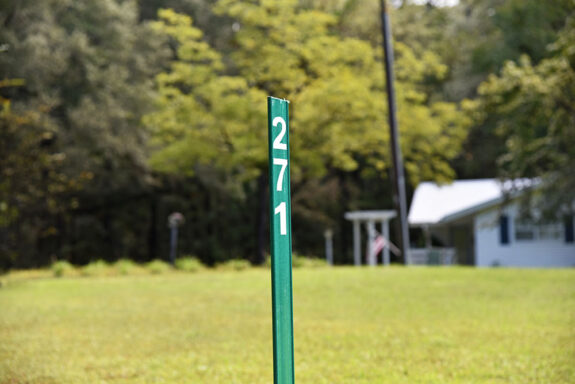 Green reflective sign with house numbers on it in yard in front of white home