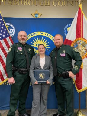 tWO UNIFORMED DEPUTIES AND ONE FEMALE IN BUSINESS ATTIRE HOLDING CERTIFICATE