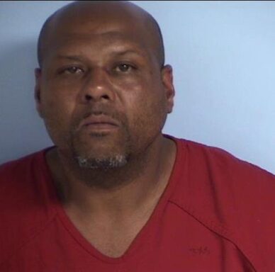 Mug shot of a black male with gray and black facial hair wearing an orange jump suit.