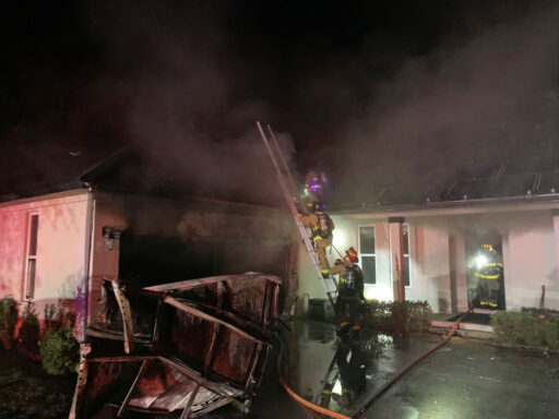 Firefighters on ladder in front of garage of burning home