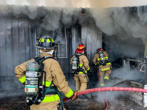 Three firefighters entering smoke-filled home