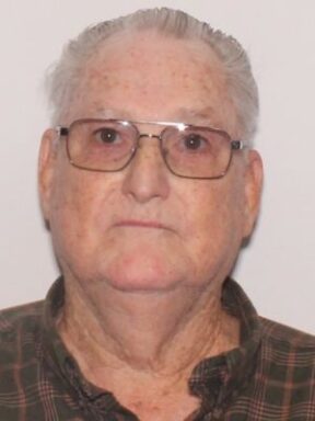 Elderly white male wearing glasses and a brown shirt